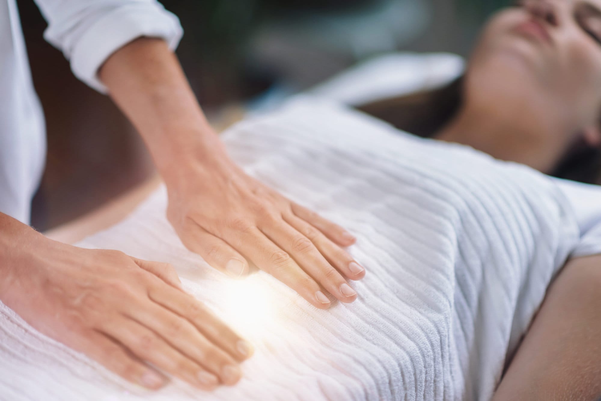 Female therapist performing Reiki therapy treatment holding hands over woman's stomach. Alternative therapy concept of stress reduction and relaxation.
